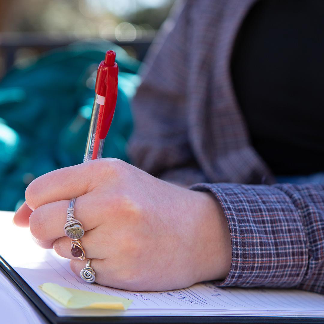 student writing on a notepad outside